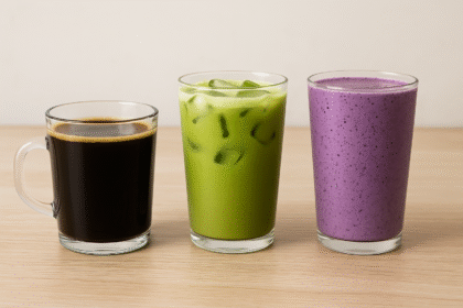 A black coffee, an iced matcha latte, and a blueberry smoothie arranged in clear and matte glassware on a white marble kitchen countertop, with soft natural lighting highlighting their vibrant colors and textures.