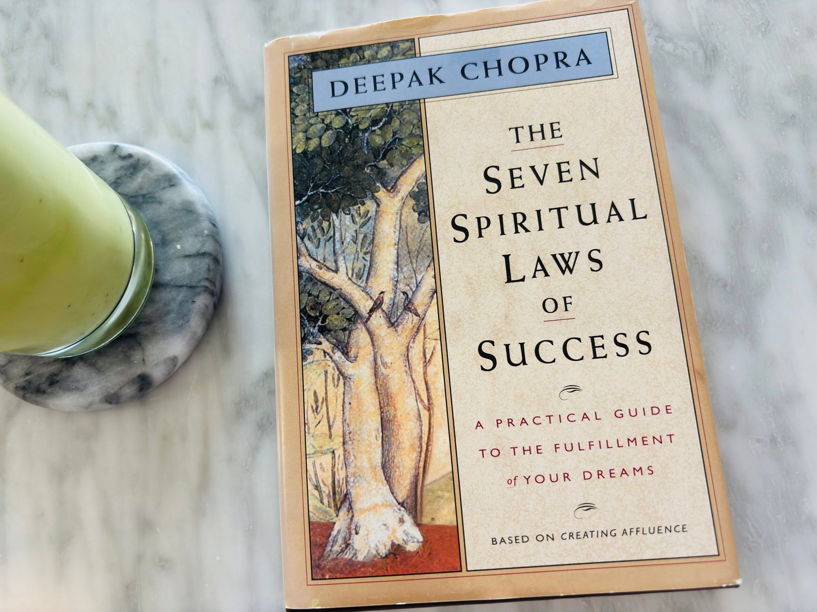 The Seven Spiritual Laws of Success by Deepak Chopra placed on a marble table next to a glass of iced matcha latte