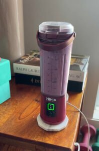 Ninja portable blender filled with a purple smoothie, sitting on a wooden desk next to books