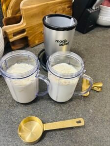 Magic Bullet blender with two filled cups of milk and protein powder beside gold measuring spoons