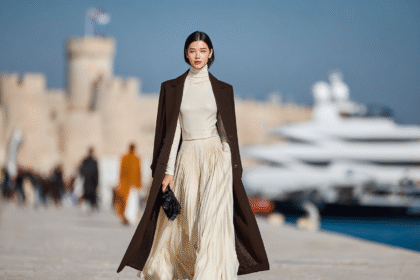 Elegant woman walking in runway-inspired outfit with pleated skirt and coat near luxury marina
