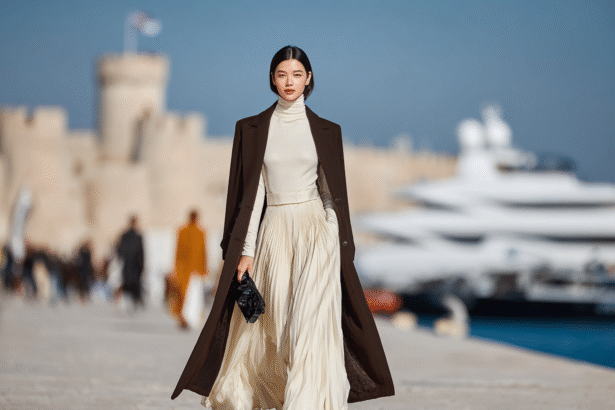 Elegant woman walking in runway-inspired outfit with pleated skirt and coat near luxury marina