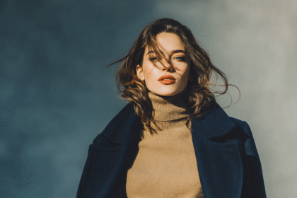 Woman in neutral turtleneck and navy coat posing confidently with windblown hair