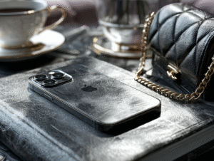 Close-up of a black Chanel flap bag with gold chain, iPhone, and leather journal on a table with elegant tea set