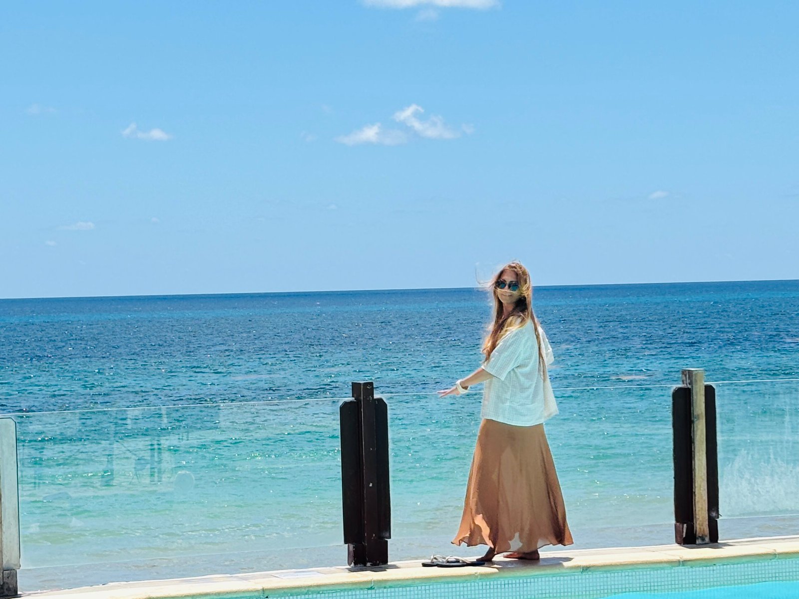 Woman in long skirt by infinity pool overlooking turquoise ocean in Cancun.