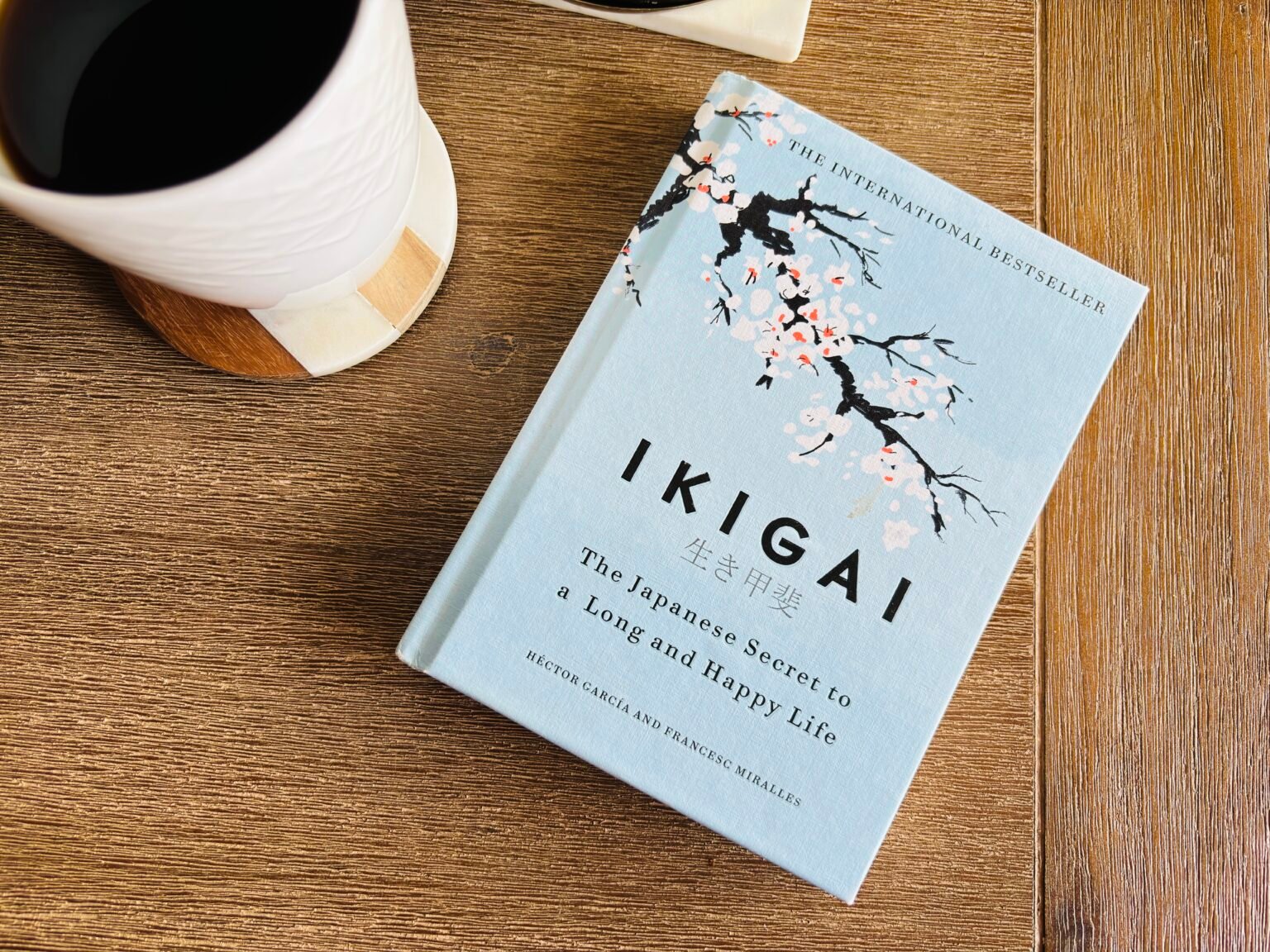 Flat lay of the book Ikigai next to a coffee mug on a wooden table