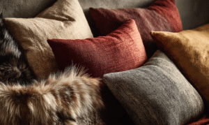 Close-up of layered designer cushions in velvet, fur, and linen textures — warm rust, gold, and taupe tones from Elegant & Driven’s Luxury Cushions Edit.
