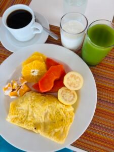 A plate of tropical fruits and an omelet served with coffee and green juice at a beach resort.