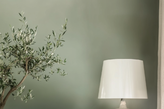 Elegant minimalist living room with soft green walls, velvet sofa, sculptural table lamp, and greenery creating a warm, refined space.