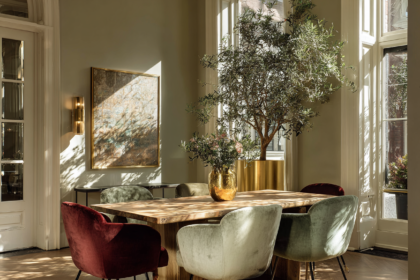 wood dining table with velvet chairs in a sunlit elegant dining room with plants and warm tones