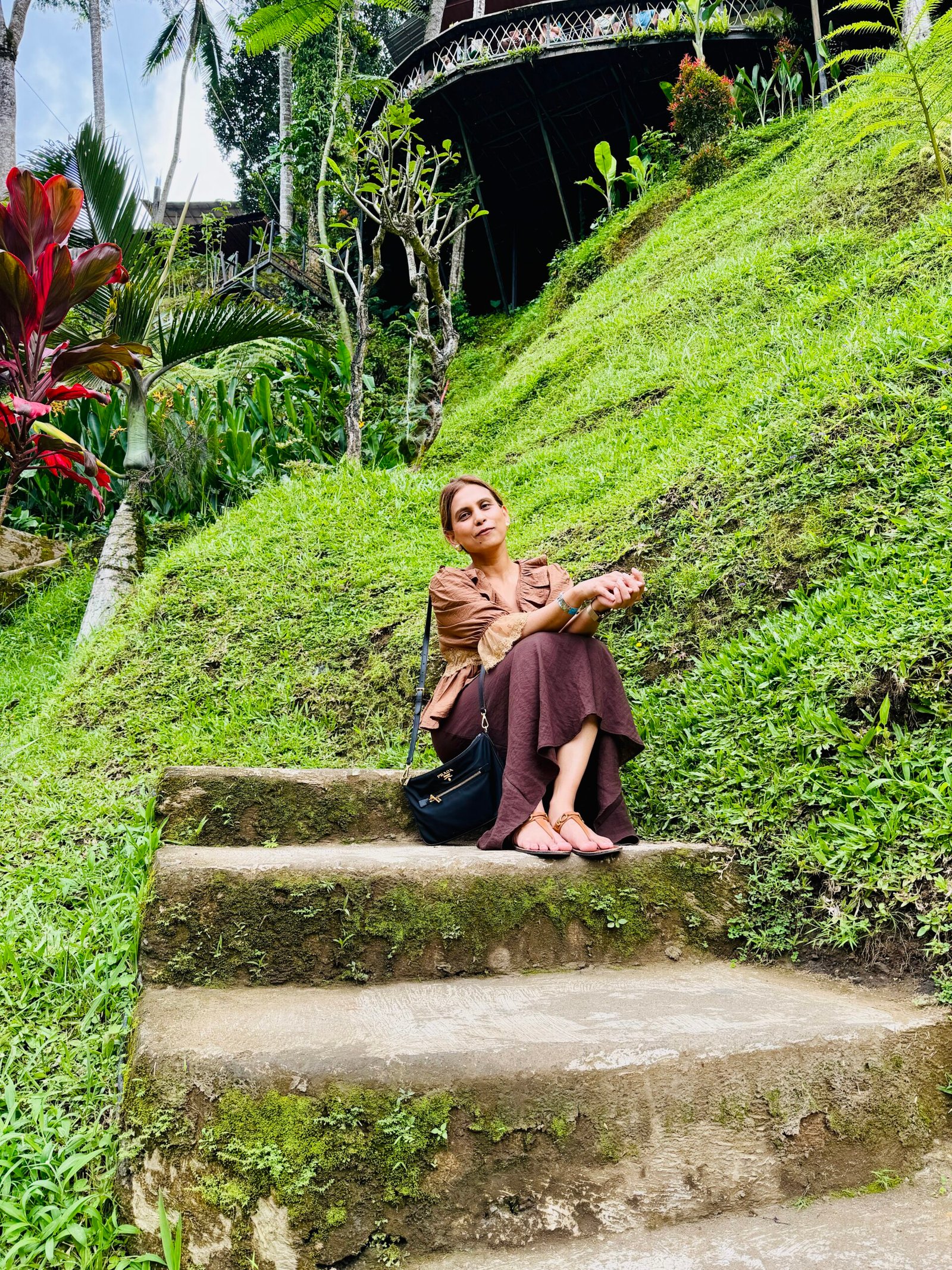 Woman sitting peacefully on stone steps surrounded by lush tropical greenery in Bali, reflecting on freedom, slow living, and personal growth.